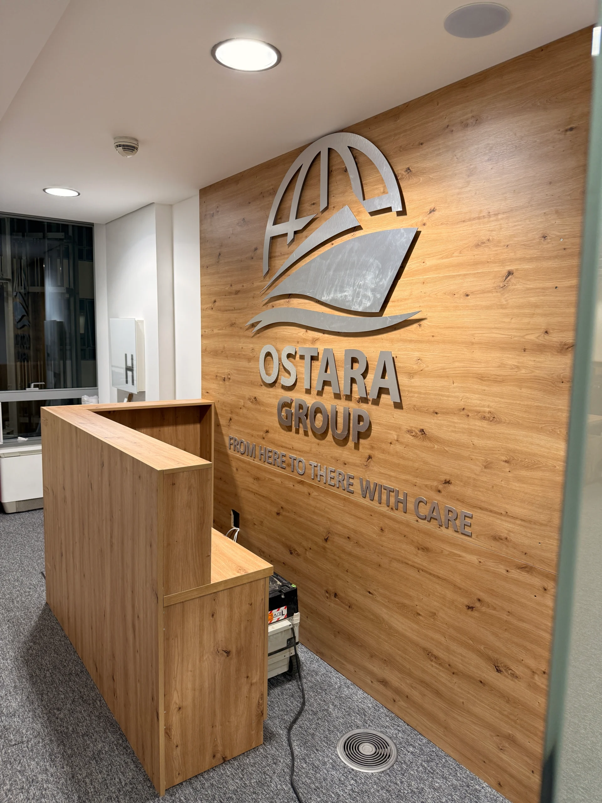 Recepcija polovnog prostora po meri, drvena obloga yida sa metalnim logom kompanije Ostara Group